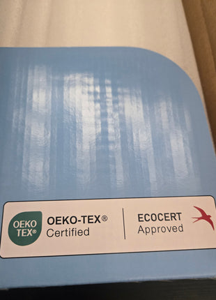 A close-up of a blue fabric sample or swatch card with rounded corners, featuring an OEKO-TEX and ECOCERT certification label at the bottom.